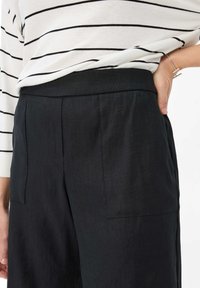 Pantaloni neri su misura con una texture liscia e una vita alta. Presentano due tasche laterali e pieghe sottili per un dettaglio in più.