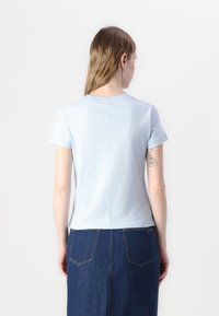 Helehelesinine lühikeste varrukatega t-särk, ümmargune kaelus, sile tekstuur ja keskel selja peal õmbluse detail, kantud denimseelikuga.