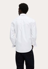 Weißes Hemd mit langen Ärmeln und klassischem Kragen. Verfügt über einen Rückenfalte und abgerundeten Saum. Kombiniert mit dunklen Denim-Hosen.