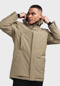 Beige wasserfester langer Anorak mit Kapuze, ausgestattet mit zwei Vordertaschen und einem Reißverschluss. Strukturierter, isolierter Stoff für Wärme.