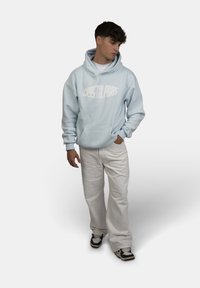 Felpa azzurro chiaro con tasca frontale e logo bianco "CRYSTAL PARKS", abbinata a pantaloni bianchi e sneakers nere e bianche.