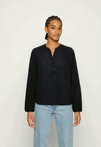 Blusa azul-marinho de mangas longas com decote redondo, apresentando bolinhas brancas, botões à frente e um corte solto. Textura do tecido suave.