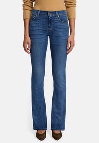Uitlopende blauwe denim jeans met een lichte wassing, vijf zakken, een sluiting met knoop aan de voorkant en subtiele stikdetails. Draagt bijpassende puntige pumps met luipaardprint.