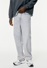 Jeans in denim grigio chiaro con una vestibilità rilassata, caratterizzati da una finitura testurizzata sottile e un classico design a cinque tasche. Abbinati a scarpe sportive.