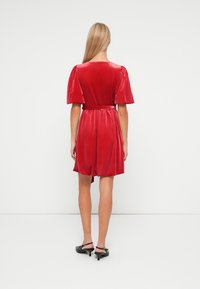 Rode fluwelen jurk met korte pofmouwen, getailleerde taille en gepuffte rok. Gladde textuur, lengte tot boven de knie, achterkant.