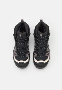 Les chaussures de randonnée noires présentent un dessus texturé, un col rembourré, des accents gris contrastants, et une semelle en caoutchouc noir durable avec protection des orteils.