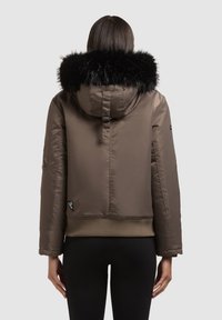 Ruskea lyhyt takki, jossa musta tekoturkistuvi, resorit helmassa ja hihansuissa, sileä pinta ja etiketti vasemmassa alareunassa.