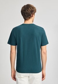 Maglietta a maniche corte color turchese con collo a giro, realizzata in un tessuto texturizzato, caratterizzata da un orlo dritto e cuciture minimali sul retro.