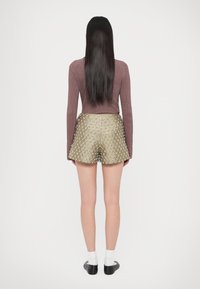 Geripptes langärmeliges Oberteil in Burgund, kombiniert mit metallisch goldfarbenen Shorts mit Diamantmuster und silbernen Akzenten. Schwarze Schuhe und weiße Socken.