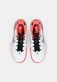 Beli športni čevlji s teksturirano zgornjo površino, črnimi vezalkami in izrazitimi koralnimi poudarki na podplatu in notranji strani, ter srebrnim logotipom.