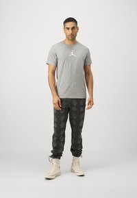 Grå Jordan-logo t-skjorte, svarte joggebukser med slangeskinnmønster, og høyde sneakers i beige med hvite såler. Avslappet atletisk stil.