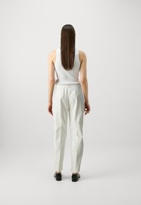 White, tailored pants with a smooth texture, featuring side pockets and a minimalist design, paired with a fitted white tank top.