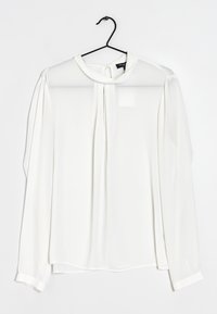 Blusa bianca a maniche lunghe realizzata in tessuto leggero e morbido. Caratterizzata da un colletto rotondo, dettagli plissettati e chiusura con bottoni sul retro.