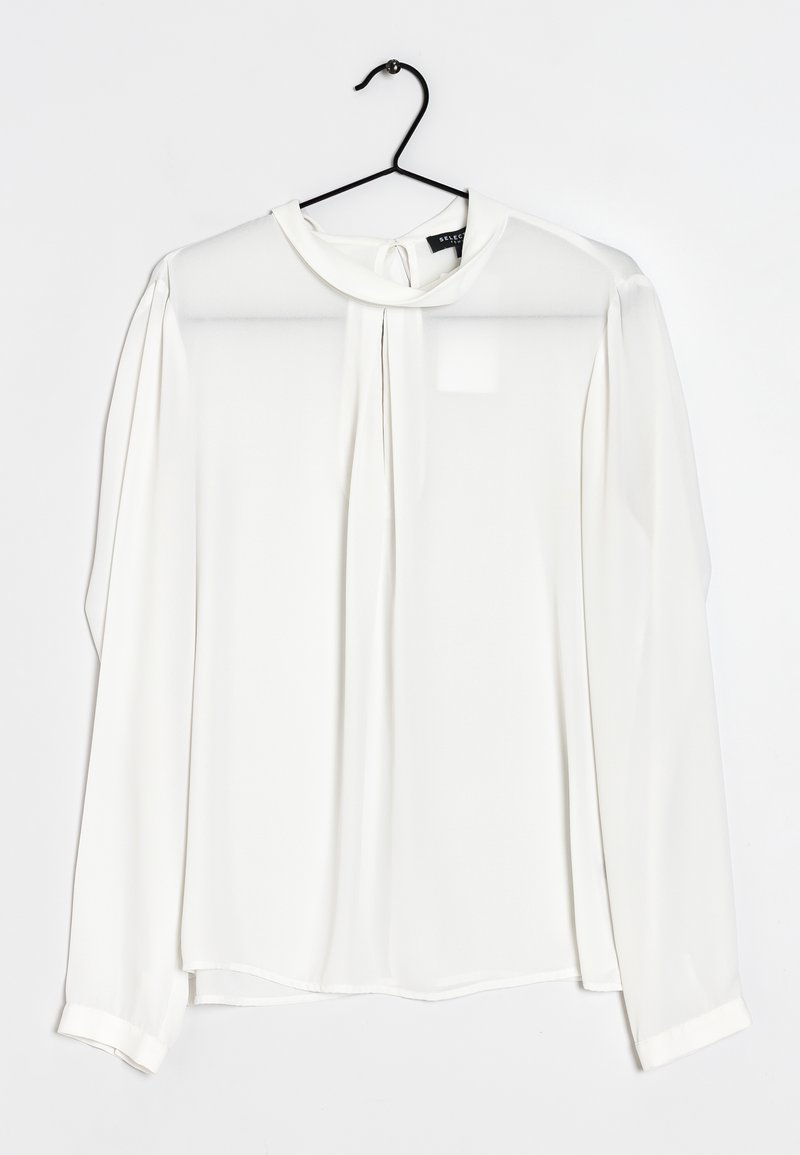 Blusa bianca a maniche lunghe realizzata in tessuto leggero e morbido. Caratterizzata da un colletto rotondo, dettagli plissettati e chiusura con bottoni sul retro.