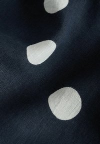 Tissu bleu foncé à gros pois blancs, montrant un tissage texturé et des plis doux créant des ombres.