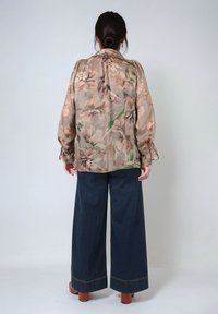 Blumenbluse aus leichtem, durchscheinendem Stoff mit Pfirsich- und Grüntönen, kombiniert mit weit geschnittenen, dunkelblauen Jeans und braunen Blockabsatzschuhen.