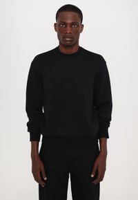 Juodas crew-neck sportinis svarkas su ilgomis rankovėmis, pagamintas iš lygaus audinio; turi raibotus rankogalius ir apatinę dalį, minimalus ženklinimas.