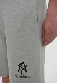Gray cotton shorts featuring a black "No Problemo" logo at the hem, with a relaxed fit and side pockets for functionality.