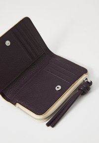 Portefeuille en cuir violet avec fermeture éclair, comportant des emplacements pour cartes, un bouton-pression et une doublure beige contrastante. Texture lisse et design structuré.