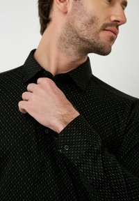 Zwarte button-up shirt met een subtiel patroon, gemaakt van soepel stof. Beschikt over een puntige kraag en knoopmanchetten met zwarte knopen.