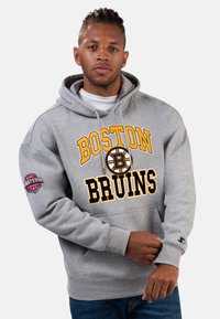Grauer Kapuzenpullover mit "BOSTON BRUINS" in gelber und schwarzer Schrift, einem Logo und einem Ärmel-Patch. Der Stoff wirkt weich und hat eine lockere Passform.