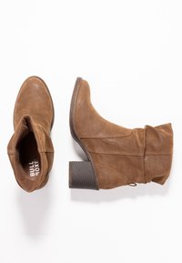 Bottes basses en daim marron avec bout arrondi et design décontracté. Dotées d'un talon empilé et de délicats accents de couture. Nom de la marque visible à l'intérieur.