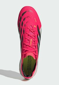 Φωτεινό ροζ ποδοσφαιρικό παπούτσι με μαύρες λεπτομέρειες, κορδόνια και λευκή σόλα, αποτυπωμένο από πάνω που δείχνει κείμενο τυπωμένο στο εσωτερικό του παπουτσιού.