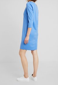 Blauwe katoenen jurk met driekwartmouwen, ontspannen pasvorm, knielang, met een ritssluiting aan de achterkant en een gladde textuur. Gedirigeerd met witte sneakers.