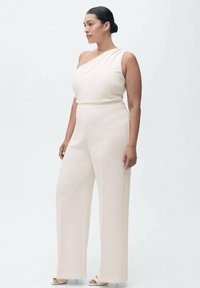En axelbärande jumpsuit i ljusbeige tyg med en figurnära överdel och vida byxor. Slät textur, minimalistisk design och inga synliga detaljer.