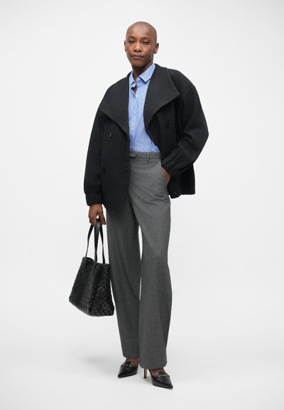 Abrigo de lana negro con cuello de chal, camisa a rayas azul y blanca, pantalones grises con estampado, bolsa de mano de mimbre negra y tacones negros de punta.