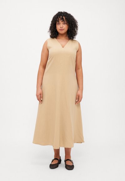 Robe sans manches couleur beige avec un décolleté en V, silhouette en A fluide, détails sur les coutures latérales et longueur au genou, associée à des chaussures plates noires.