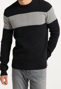 Schwarzer Strickpullover mit einem horizontalen grauen Streifen über der Brust. Rippbündchen und Saum, strukturiertes Design mit variierender Stichtiefe.