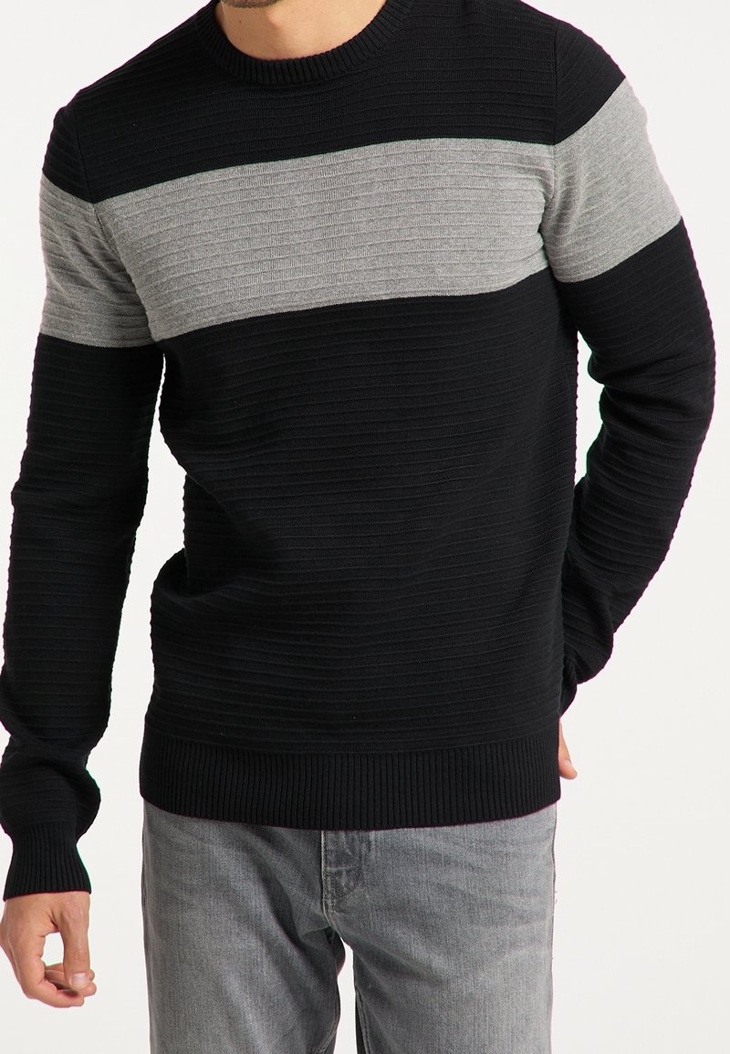 Schwarzer Strickpullover mit einem horizontalen grauen Streifen über der Brust. Rippbündchen und Saum, strukturiertes Design mit variierender Stichtiefe.