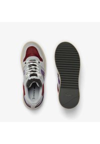 Sneakers Lacoste con tomaia grigia, rossa e viola. Presentano una pelle scamosciata testurizzata, dettagli in mesh, lacci bianchi e una suola in gomma con scanalature.
