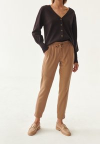Mørkelilla cardigan med V-hals og knaplukning, parret med lysebrune bukser med snoretræk og beige loafers med guldakcenter.