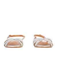 Flat sandals featuring crisscross silver straps, tan ankle straps, a smooth tan footbed, and a simple buckle closure.