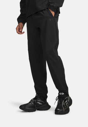 Czarne spodnie sportowe o zwężanym kroju, wykonane z lekkiego materiału, połączone z czarnymi trampkami z srebrnymi akcentami i teksturowanym wzorem.