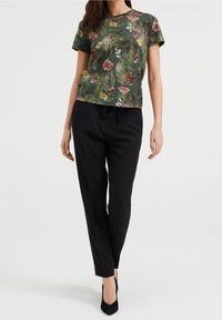 Květnový zelený top s krátkými rukávy, zdobený růžovými, žlutými a bílými kv ětinami. Spárován s černými zúženými kalhotami a lodičkami.