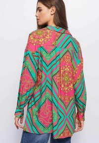 Camisa de manga larga con un vívido patrón en tonos rosa, turquesa y dorado, que presenta diseños geométricos y florales; corte relajado y tejido suave.