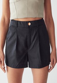 Černé šortky s upraveným designem, s viditelným předním knoflíkem a detailem skladů, vyrobené z hladké, lehké látky.