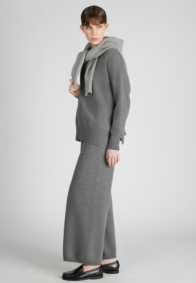 Grau gestrickter Pullover über einem passenden langen Rock, beide aus einem weichen Material. Das Outfit wird mit schwarzen Schuhen und einem hellgrauen Schal abgerundet.