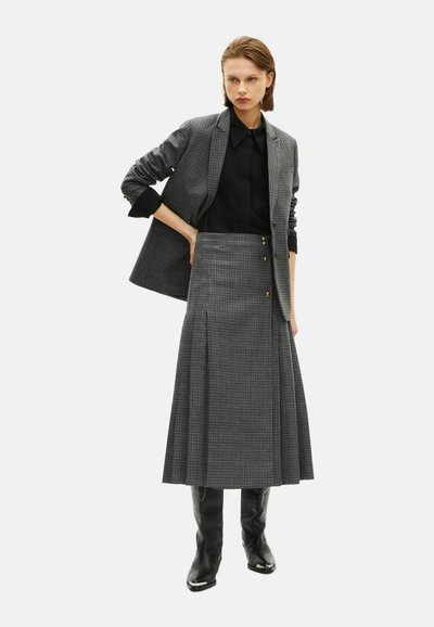 Blazer et jupe à carreaux gris, blouse noire, design jusqu'au genou, plis, boutons dorés, associés à des bottes noires jusqu'au genou.