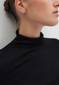 Schwarzes, geripptes Rollkragenoberteil mit taillierter Passform. Nahaufnahme zeigt eine glatte Textur und einen hohen Kragen, der einen minimalistischen Stil betont.