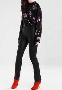 Haut à manches longues noir à fleurs avec des fleurs roses et blanches, associé à un pantalon en cuir noir moulant avec des fentes sur les côtés et des talons aiguilles rouges.