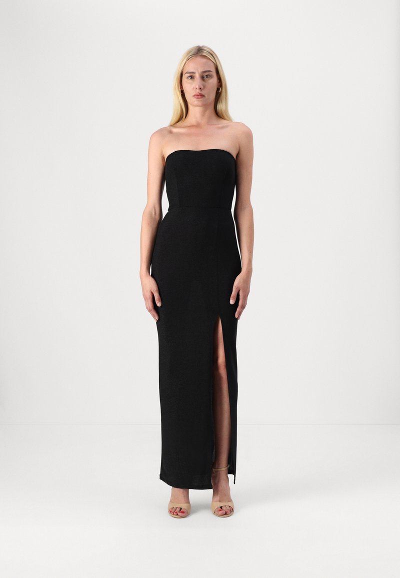 Črna brezramna obleka z oprijetim zgornjim delom in visokim razporkom na eni strani, izdelana iz teksturirane tkanine, v kombinaciji z nude petkami.