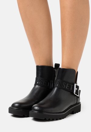 Stivaletti neri in pelle con suola spessa, dotati di una cerniera laterale e di una fascia decorativa con testo impresso. Texture liscia.