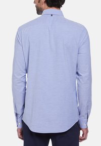 Lichtblauwe lange mouw shirt van zacht materiaal, met een klassieke kraag, knopenmanchetten en een gebogen zoom. Subtiele textuurdetails.