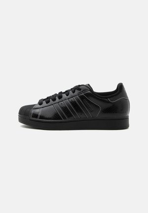 Schwarzer Sneaker mit niedrigem Schnitt aus strukturiertem Leder, drei Streifen an der Seite, schwarzen Schnürsenkeln und einer Gummischalensohle am Vorderfuß.