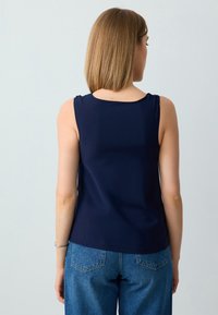 Top senza maniche di colore blu navy con una texture liscia e scollatura arrotondata, abbinato a jeans in denim a vita alta e un semplice braccialetto d'argento.