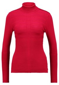 Pull à col montant rouge en matière lisse et extensible, avec des accents à côtes horizontales sur la poitrine et des côtes verticales au niveau de l'ourlet.